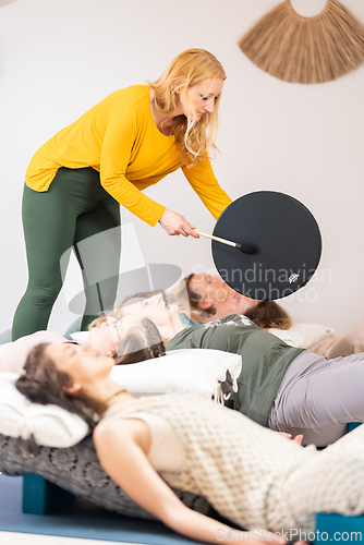 Image of Group therapy session with Tibetan drum for group of women lying on wooden floor surrounded by copper bowls. Meditation and relaxation