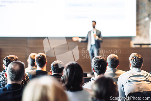 Image of Speaker giving a talk in conference hall at business event. Rear view of unrecognizable people in audience at the conference hall. Business and entrepreneurship concept.