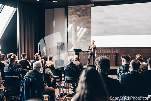 Image of Speaker giving a talk in conference hall at business event. Rear view of unrecognizable people in audience at the conference hall. Business and entrepreneurship concept.