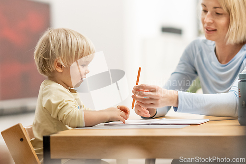 Image of Caring young Caucasian mother and small son drawing painting in notebook at home together. Loving mom or nanny having fun learning and playing with her little 1,5 year old infant baby boy child.