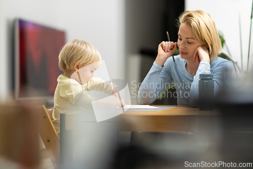 Image of Caring young Caucasian mother and small son drawing painting in notebook at home together. Loving mom or nanny having fun learning and playing with her little 1,5 year old infant baby boy child.