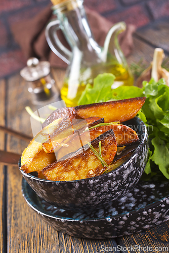 Image of Bowl with baked potatoes on wooden background
