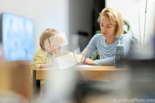 Image of Caring young Caucasian mother and small son drawing painting in notebook at home together. Loving mom or nanny having fun learning and playing with her little 1,5 year old infant baby boy child.