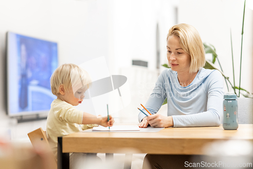 Image of Caring young Caucasian mother and small son drawing painting in notebook at home together. Loving mom or nanny having fun learning and playing with her little 1,5 year old infant baby boy child.