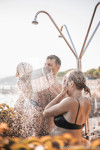 Image of Mom, dad and their toddler child under a tropical shower. Parents with their cute infant boy playing on the beach under shower water splashes. Playful moment at summer family holiday.