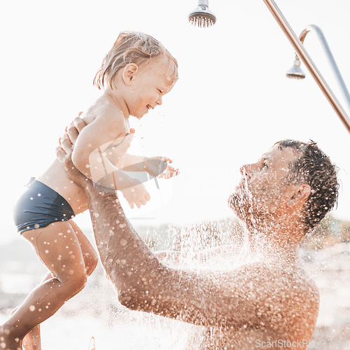 Image of Dad and baby under a tropical shower. dad and his cute infant boy playing on the beach under shower water splashes - Father taking care of cute sun in playful moment at summer family holiday.