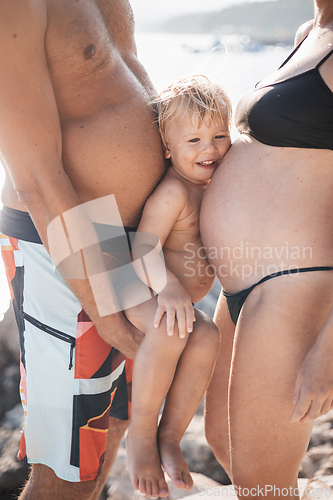Image of Funny summer family portrait of cute little smiling boy with his head squeezed between two large bellies of his parents who expect another baby.
