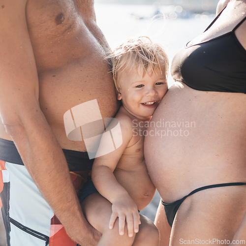 Image of Funny summer family portrait of cute little smiling boy with his head squeezed between two large bellies of his parents who expect another baby.