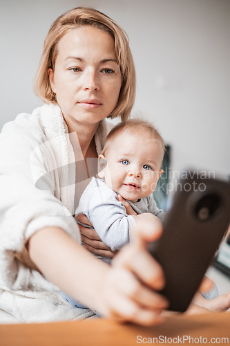 Image of Authentic shot of neo mother and her newborn baby making a video call to father or relatives with laptop on a sofa in a living room.