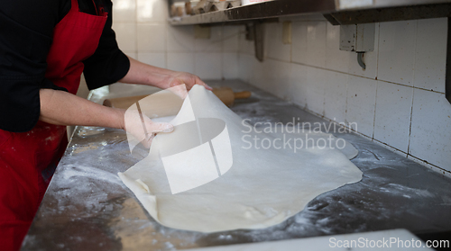 Image of Rolling out dough on floured surface in commercial kitchen