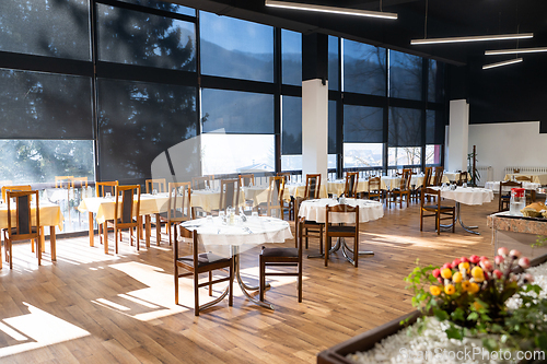 Image of Restaurant interior with large sunlit windows and wooden chairs