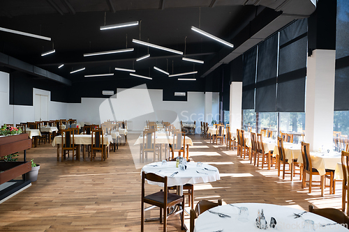 Image of Restaurant interior with large sunlit windows and wooden chairs