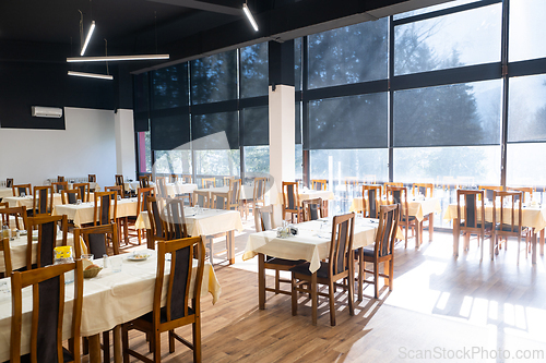 Image of Restaurant interior with large sunlit windows and wooden chairs
