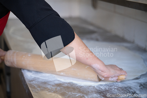 Image of Rolling out dough on floured surface in commercial kitchen