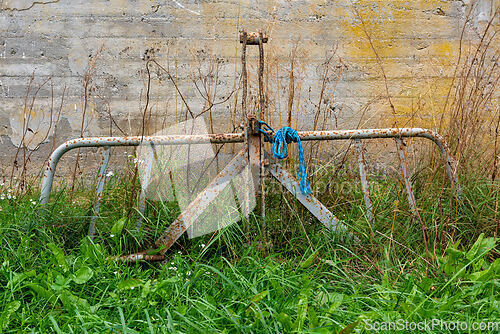 Image of Old metal farm implement rests among tall grass near a weathered