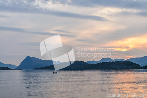 Image of Sunset over calm sea with distant mountains and a small boat in 