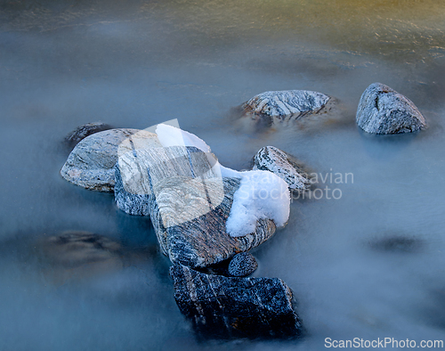 Image of Frozen stones partially covered with snow in a tranquil river un