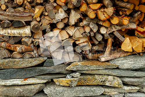 Image of Wood stacked neatly against a stone wall, showcasing natural tex