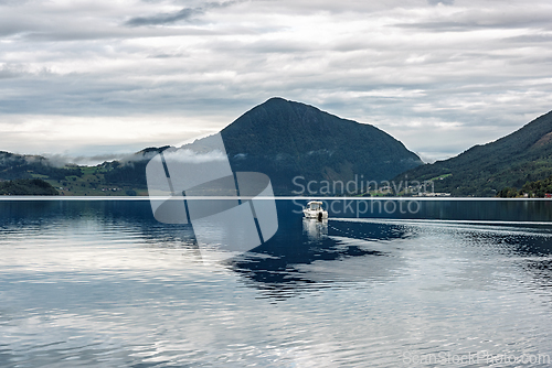 Image of Boat gliding on calm waters under cloudy skies near mountains in