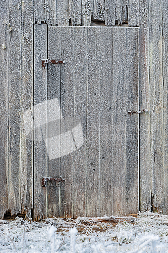Image of Frost-covered wooden door on a rustic barn surrounded by icy gra