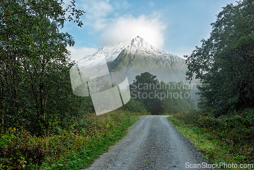 Image of Scenic gravel road leading towards a misty snow-capped mountain 