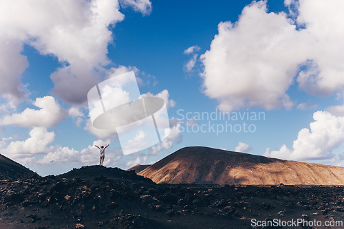 Image of Woman rising hands up in the sky, enjoying amazing views of volcanic landscape in Timanfaya national park on Lanzarote, Spain. Freedom and travel adventure concept.