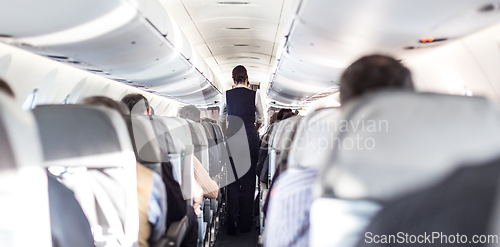 Image of Interior of airplane with passengers on seats and stewardess in uniform walking the aisle, serving people. Commercial economy flight service concept.