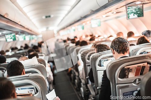 Image of Interior of airplane with passengers on seats and stewardess in uniform walking the aisle, serving people. Commercial economy flight service concept.