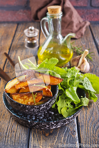 Image of Bowl with baked potatoes on wooden background