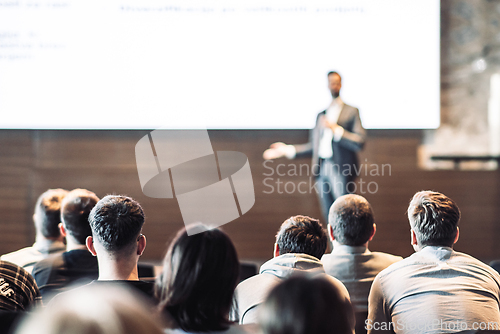 Image of Speaker giving a talk in conference hall at business event. Rear view of unrecognizable people in audience at the conference hall. Business and entrepreneurship concept.