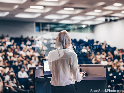 Image of Female speaker giving a talk on corporate business conference. Unrecognizable people in audience at conference hall. Business and Entrepreneurship event.