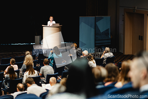 Image of Female speaker giving a talk on corporate business conference. Unrecognizable people in audience at conference hall. Business and Entrepreneurship event.