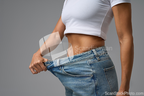 Image of Fit woman in white crop top showing weight loss success by holding loose jeans