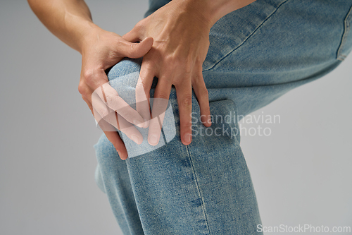 Image of Close-up of woman holding her knee feeling joint pain wearing jeans indoors