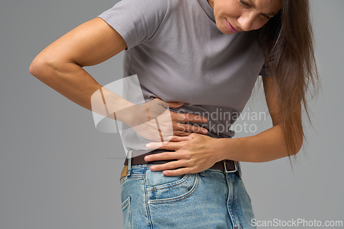 Image of Woman bending sideways and holding abdomen in pain, neutral grey studio setting