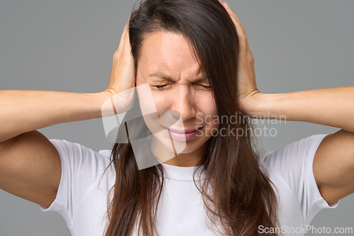 Image of Close-up of woman covering ears tightly with eyes closed in reaction to loud