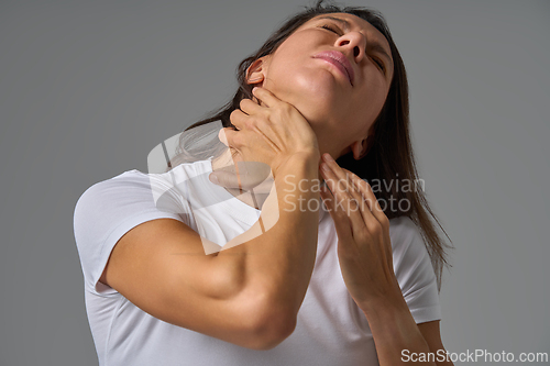 Image of Woman in white t-shirt holding neck showing pain and tension in throat indoors