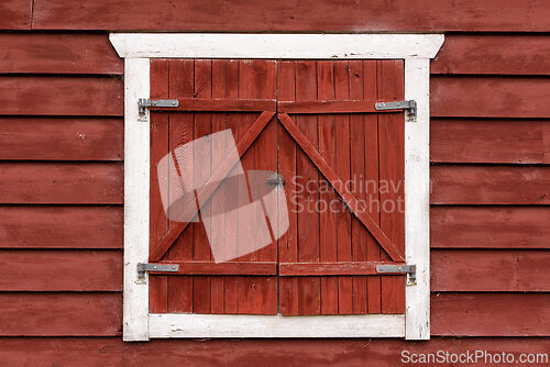 Image of Rustic wooden window with shutters on a red barn facade in a cou