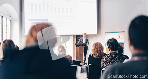 Image of Speaker giving a talk in conference hall at business event. Rear view of unrecognizable people in audience at the conference hall. Business and entrepreneurship concept.