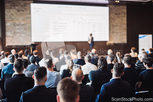 Image of Speaker giving a talk in conference hall at business event. Rear view of unrecognizable people in audience at the conference hall. Business and entrepreneurship concept.
