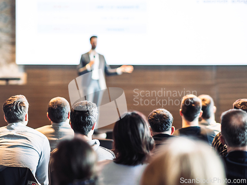 Image of Speaker giving a talk in conference hall at business event. Rear view of unrecognizable people in audience at the conference hall. Business and entrepreneurship concept.