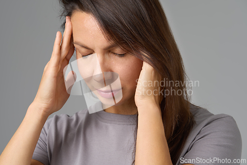 Image of Calm woman pressing temples with eyes closed in grey studio background,