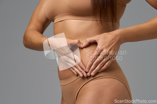 Image of Fit woman forming heart shape with hands on her flat stomach in beige underwear