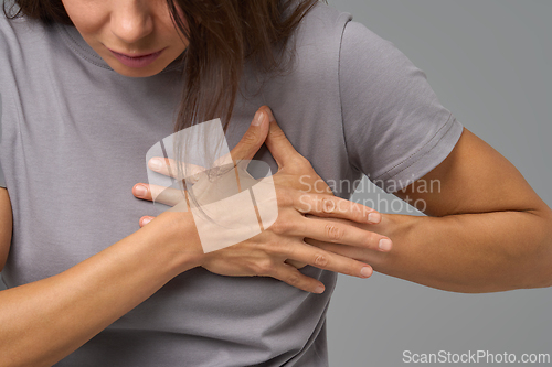 Image of Woman clutching chest in discomfort, close-up studio view on neutral grey background,