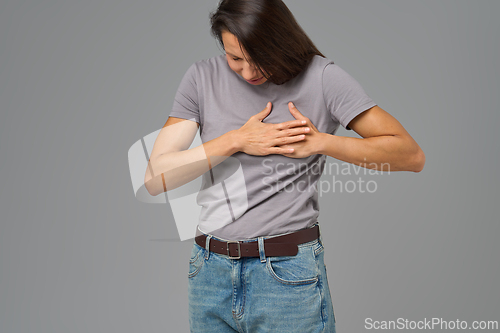 Image of Woman holding chest with both hands, bending forward in pain, neutral background