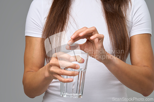 Image of Close-up of woman dropping vitamin tablet into glass of water during daily supplement routine