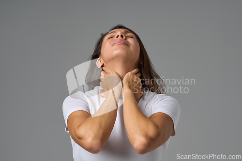 Image of Woman holding neck in pain and looking up showing tension or discomfort in throat area indoors