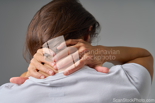 Image of Rear view of woman holding back of neck showing pain or muscle tension