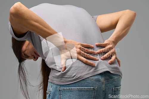 Image of Woman bending forward with hands on lower back, grimacing in pain, studio image
