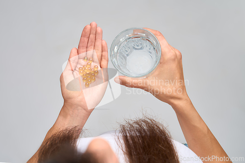 Image of Top view of woman holding glass of water and omega-3 capsules